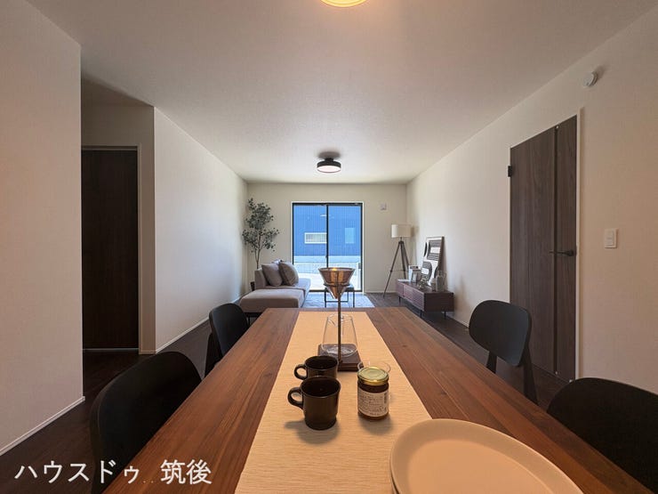 【キッチン側から見渡せるLDK】食事の準備中もリビングでくつろぐご家族と自然に会話が弾む、一体感のある配置です。奥の大きな窓から差し込む光が、空間全体を優しく明るく開放的に演出してくれます。