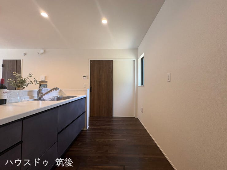 【明るく清潔感のある調理空間】手元や通路を優しく照らすダウンライトが心地よいキッチン。背面壁には小窓もあり、採光や換気にも配慮されています。日々のお料理タイムがより快適に、楽しくなる空間です。