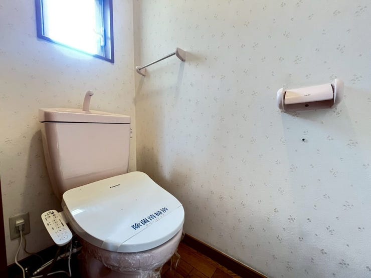 淡いピンク色の手洗い一体型タンクと温水洗浄便座が設置されたトイレです。ペーパーホルダーも同色で揃えられ、小花柄のクロスと合わせた統一感のある空間です。