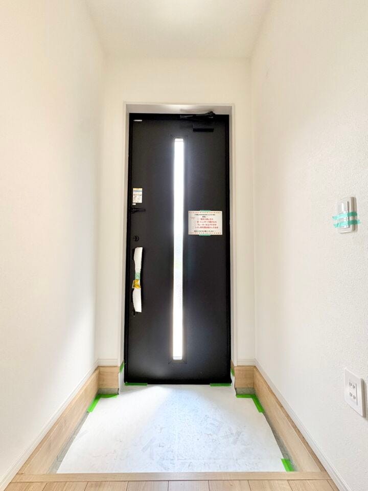 ダークカラーのドアに縦長の採光窓があしらわれており、モダンで洗練された雰囲気を感じさせます。単なる出入り口ではなく、家の顔としておしゃれなアクセントになっています。