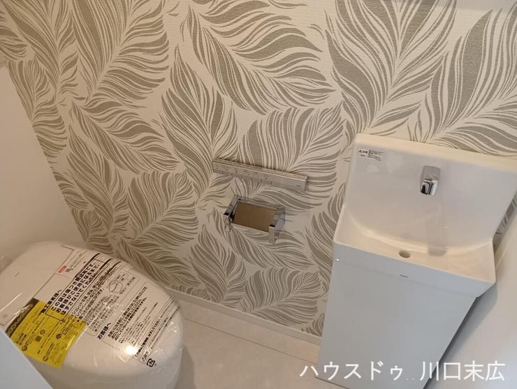 スタイリッシュな手洗いキャビネットを備えたトイレ。デザイン性の高いアクセントクロスが空間を上品に彩り、ゲストも心地よく使用できる工夫が凝らされています。