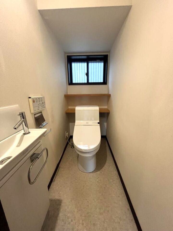 白を基調にした清潔感あるトイレ空間。窓から光が差し込み、独立手洗いと棚を備えた機能的な設えです。