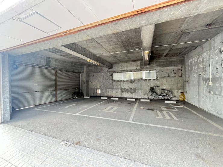 コンクリート造の建物内に設けられた駐車場です。屋根付きの構造で、床面には白線と車止めブロックが設置され駐車区画が整備されています。