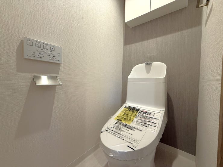 ■温水洗浄便座付きトイレ■
白を基調とした内装に、おしゃれなアクセントクロスが映える落ち着いた空間です。上部にはトイレットペーパーなどのストックをスッキリ隠して収納できる、扉付きの棚を備えています。