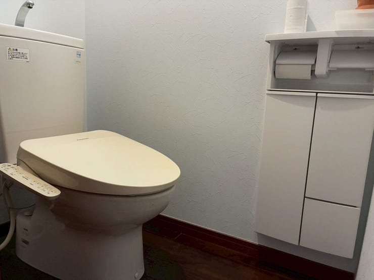 温水洗浄便座仕様のトイレです。手洗い付きタンクが備わるほか、壁面には二連ペーパーホルダーと一体化したキャビネットが設置され、衛生用品の収納スペースが確保されています。