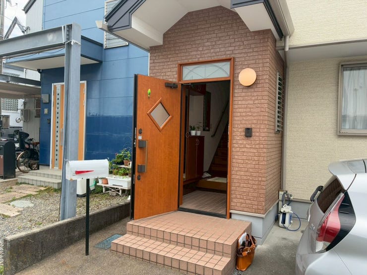 レンガ調の外壁に、小窓付きの木目調ドアが組み合わされています。足元はタイル貼りのステップ仕様で、横にはポストや照明が配置されています。