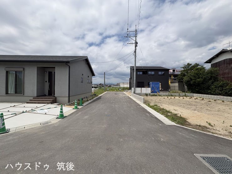 【まもなく着工予定】幅員6m公道のすっきりとした道路環境が確認できる建築前の現地写真です。この敷地内に、図面通りの並列カースペースや建物が整備されます。