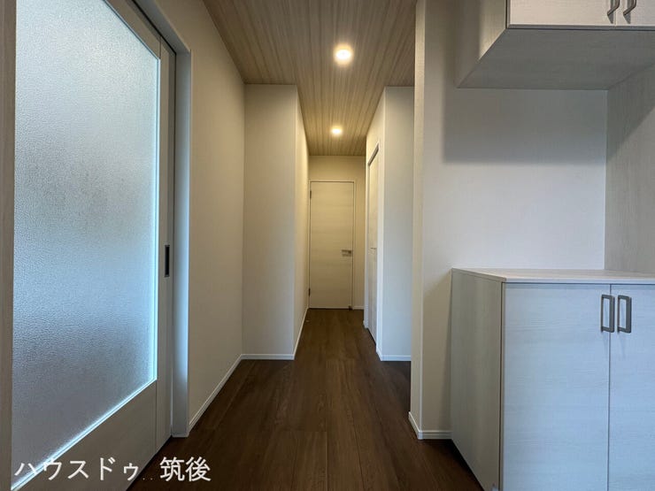 【落ち着きのある1階廊下】シックなフローリングと、ぬくもりあるダウンライトが洗練された印象を与える空間。左側にはリビングへ続くスタイリッシュなスリットガラス入りの引き戸を配しています。