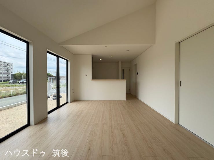 【高天井が特徴の16帖LDK】開放感のある勾配天井を採用したリビングです。奥にはご家族との会話が弾む対面式のシステムキッチンを配置。大きな窓が並び、室内にしっかりと自然光を採り込める設計です。