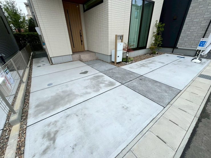 前面にコンクリート舗装の駐車スペースが確保されています。平坦な造りで複数台の駐車区画が設けられています。機能門柱が配置され、玄関への動線が整った設計です。