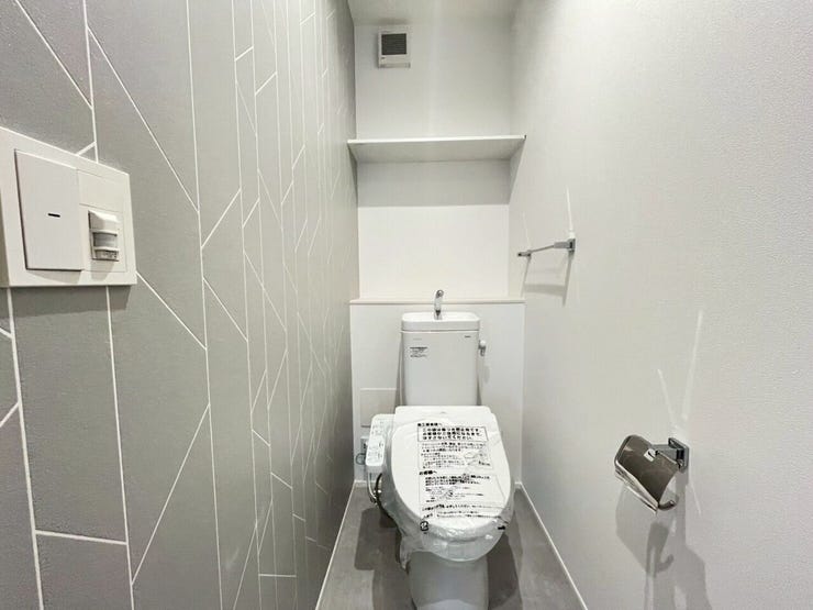 2階トイレ
グレーの幾何学的なライン柄のアクセントクロスを施したトイレです。手洗い付きのタンクや上部の収納棚、タオル掛けなどが設置されています。白とグレーを基調にすっきりとまとめられた設計です。