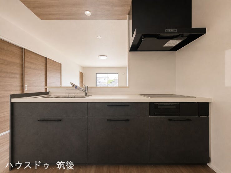 【IH仕様の対面式キッチン】料理中もリビングを見渡せる対面型。お手入れが簡単なIHクッキングヒーターを採用しています。一部の天井にあしらわれた木目調クロスが、空間のスタイリッシュなアクセントです。