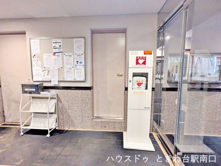万が一の時に備えたAEDが設置されています。掲示板には最新の案内があり、丁寧な管理体制が整っていることが伺えるエントランス付近です。※2026年10月まで大規模修繕工事中のため養生等がされています。