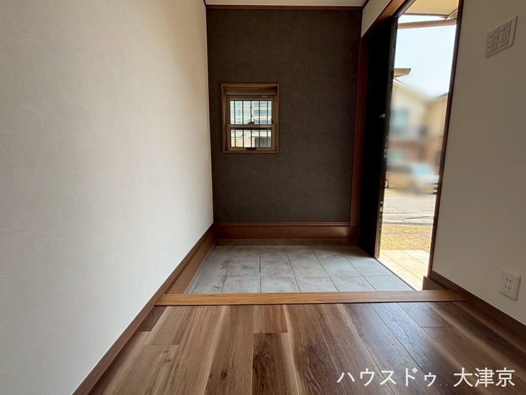 木目の上がり框と質感あるタイルが調和した玄関。シックなアクセントクロスが上質な空間を演出します。
