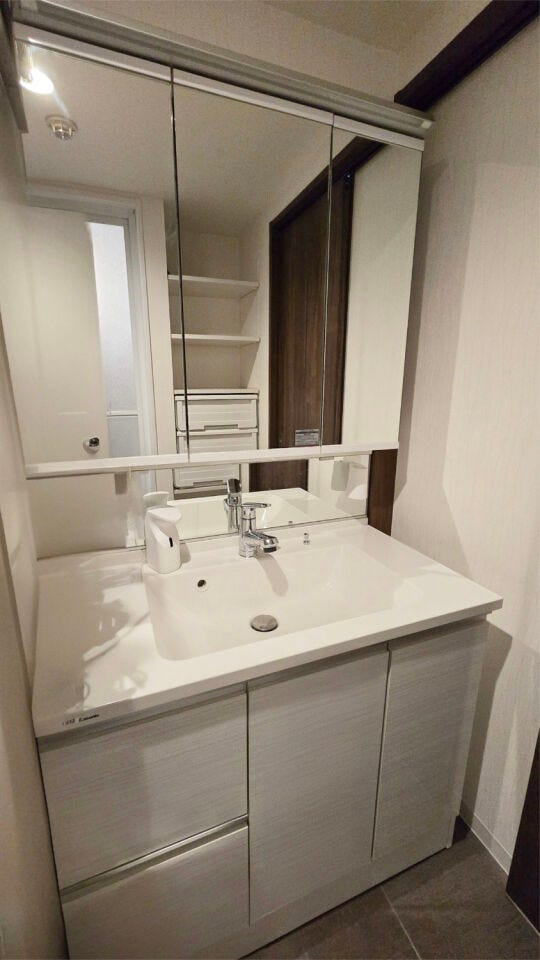 【居住中のため家具削除し、CGで加工した室内写真】清潔感あふれる洗面化粧台は、忙しい朝をサポートする明るい空間。横には洗濯機置場も確保されており、家事動線にも配慮されています。