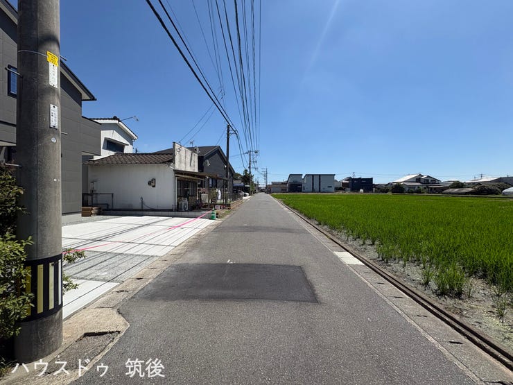 【西側接道・荒木小エリア】見通しの良い道路環境に面した現地写真です。周辺は緑が広がる落ち着いた街並み。車2台分の駐車スペースを備えた8月完成予定の新築4LDKです。ぜひ現地でお確かめください。