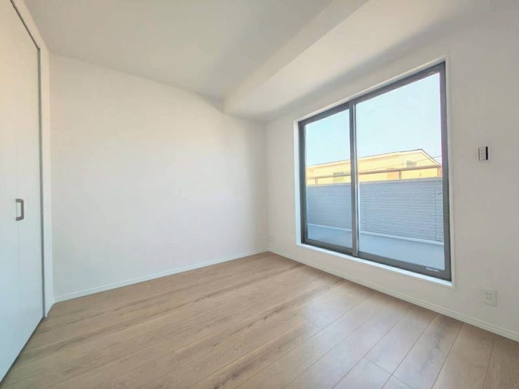 白を基調とした壁と明るい木目調の床が爽やかな洋室です。バルコニーへ繋がる大きな窓が配置され、室内に開放感をもたらす構造になっています。クローゼットの扉も白で統一され、すっきりとしたデザインです。
