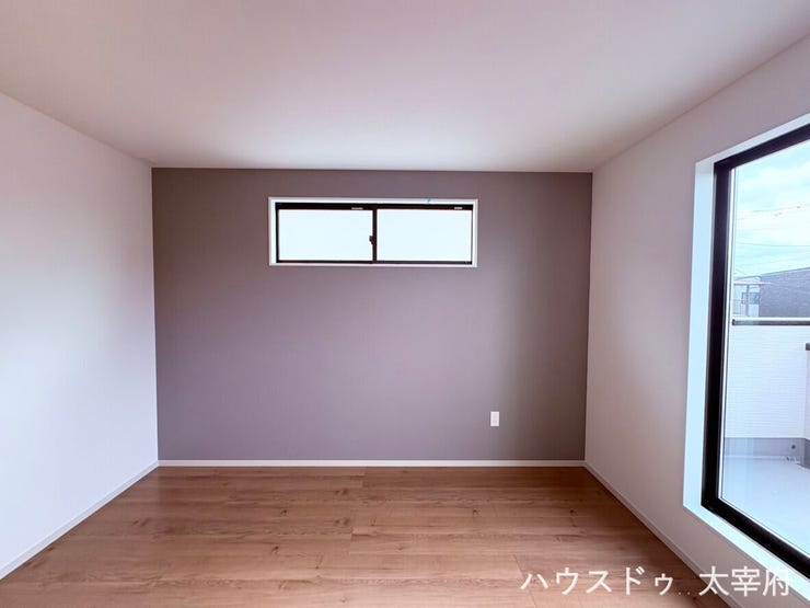 【2F/8帖洋室】落ち着いたアクセントクロスが印象的な、上品でモダンな洋室です。木目調のフロアと大きな窓から差し込む明るい自然光が心地よく、開放感とプライベート感を両立したリラックスできる空間です。