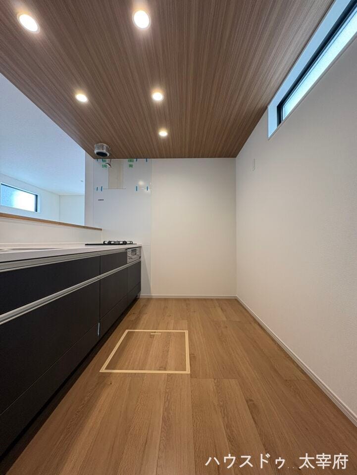木目調の美しい天井とダウンライトがスタイリッシュな空間を演出。落ち着いた黒のシステムキッチンは収納力が高く、すっきりとした機能的な調理スペースを実現します。背面に高窓もあり採光も確保されています。