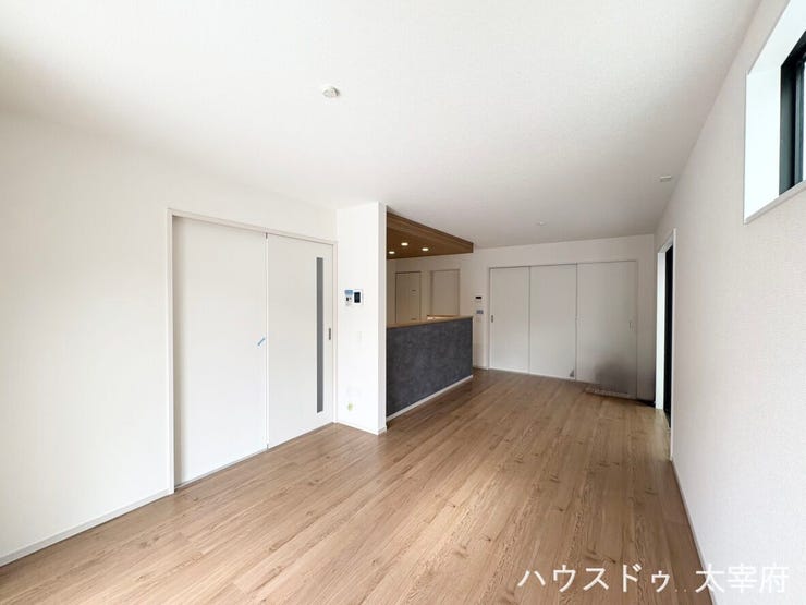 木目調のフロアと白い壁が調和する、明るく開放的なLDKです。奥に見えるグレー調のカウンターキッチンがおしゃれなアクセントとなり、家事動線とデザイン性を兼ね備えた心地よい空間です。
