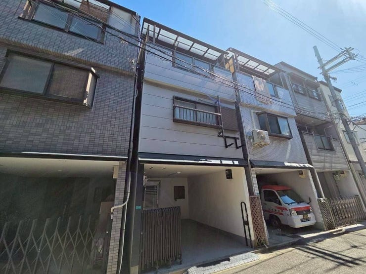 すっきりとしたグレーの現代的な外壁デザイン。限られた敷地を有効に活かした縦長構造の3階建てで、1階部分には雨や日差しから自家用車や自転車を守る、屋根付きの駐車・駐輪スペースが確保されています。