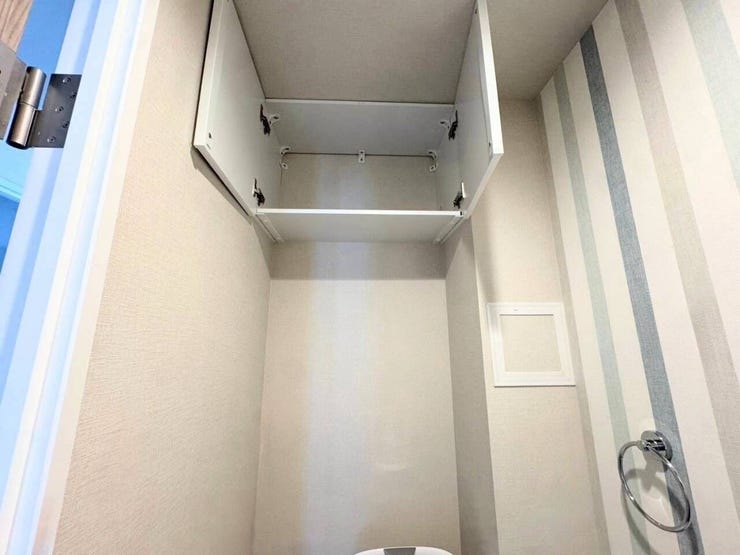 トイレットペーパーのストックや掃除用品をスッキリ収納できる、便利な吊戸棚を備えたトイレ空間です。爽やかなストライプ柄のアクセントクロスが、スタイリッシュで清潔感のある雰囲気を演出しています。