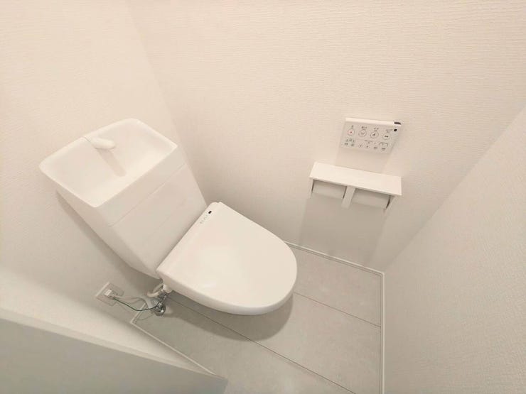 手洗い一体型の温水洗浄便座付きトイレ。壁面リモコンや、スマホ・芳香剤が置けるカウンター付きペーパーホルダーを設置。白で統一された空間が清潔で心地よい印象を与えます。
