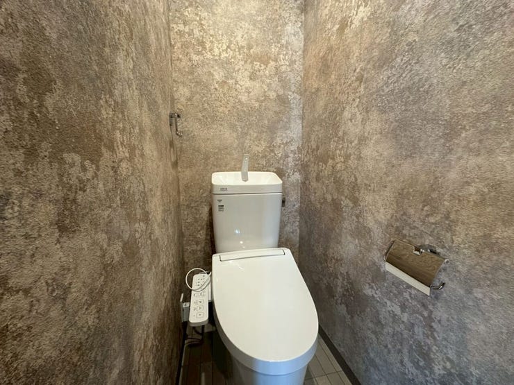 モルタル風のデザインクロスが壁一面に施されたスタイリッシュなトイレ空間です。落ち着いた質感と色合いが上質な雰囲気を作り出し、シックでモダンな印象を与えます。