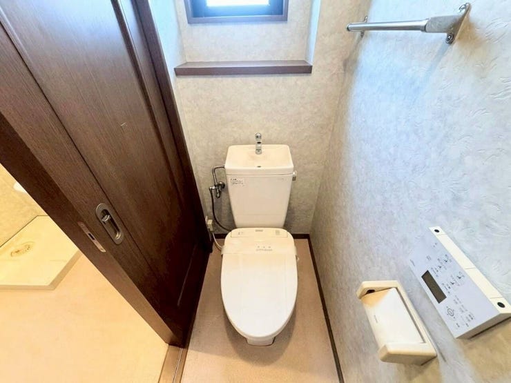 手洗い付きタンクと温水洗浄便座を備えたお手洗いです。小窓があるため自然換気が行いやすく、いつでも爽やかな空間を保てます。壁面のリモコンやタオル掛けなど、日常使いの利便性にも配慮されています。