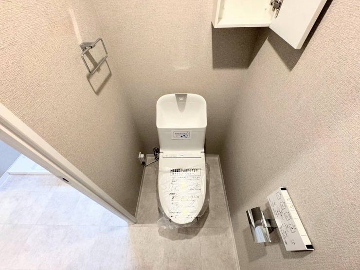 落ち着いたグレージュの壁紙で整えられたトイレ空間。手洗い付きの温水洗浄便座に、操作しやすい壁付けリモコンを完備しています。上部にはトイレットペーパーなどを隠して収納できる便利な吊戸棚付きです。