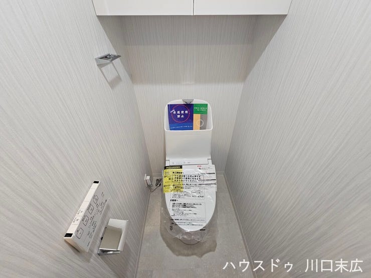 温水洗浄便座と上部吊戸棚を備えたトイレ空間。トイレットペーパーや清掃用品をスッキリと収納できます。