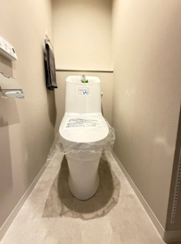淡いニュアンスカラーのクロスと石目調フロアが上品なトイレ空間。手洗い・温水洗浄機能付きで、ペーパー類を置ける便利なカウンター棚も備えています。