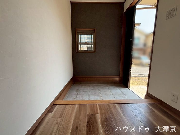 木目の上がり框と質感あるタイルが調和した玄関。シックなアクセントクロスが上質な空間を演出します。