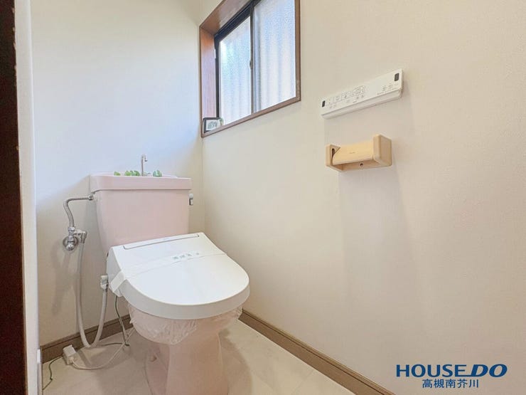 温水洗浄便座を完備した清潔感漂うトイレです。壁面には便利なリモコンとペーパーホルダーが配置され、窓からの採光と換気でいつでも気持ちよく利用できます。