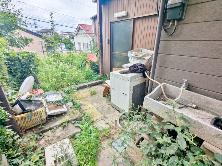 屋外の流し台や洗濯機が残る建物脇の様子です。残置物を含めた現況を、ご見学の際にお確かめください。