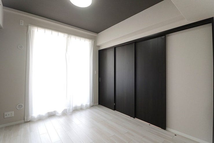 大きな窓から自然光が差し込む、明るい洋室です。壁一面の大きな引き戸収納は、お部屋をすっきりと広く保つのに役立ちます。清潔感のあるフローリングと落ち着いた色の天井で、くつろぎの空間が広がります。