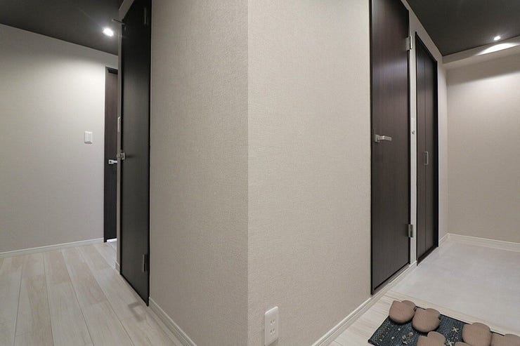 玄関から続く廊下は、白とダークブラウンのコントラストが美しい洗練された空間。各居室への動線がスムーズで、プライバシーにも配慮された間取りです。天井のライトが空間を柔らかく照らします。