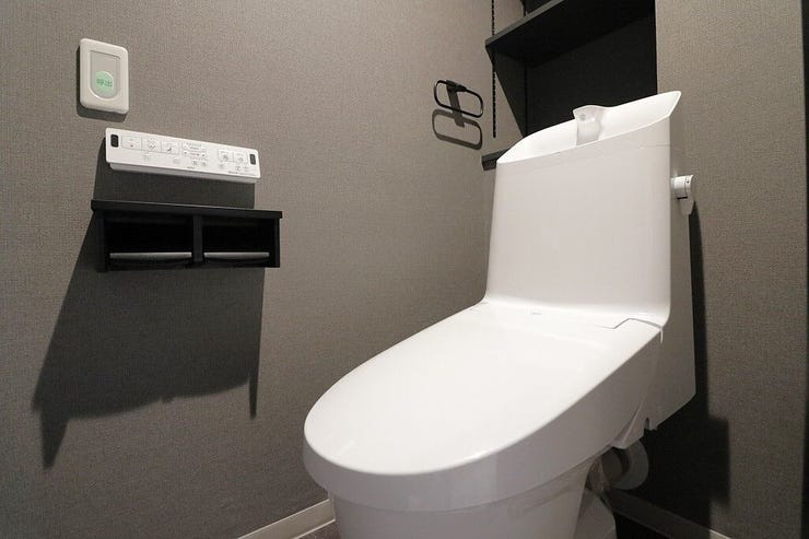 シックなグレーのクロスが落ち着いた雰囲気を演出するトイレ空間。お手入れしやすい手洗い一体型を採用しています。壁掛けリモコンや小物が置ける二連ペーパーホルダーを備えており、毎日の使い勝手も良好です。